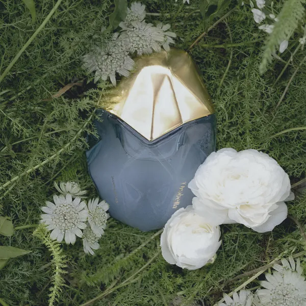 Orebella Jasmine Blues parfüümipudel lillede ja roheluse keskel.