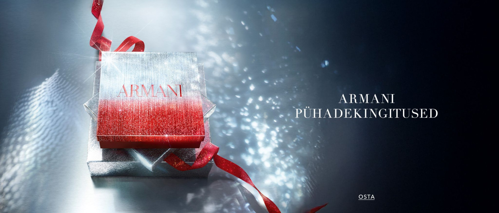Hõbedane ARMANI kinkekarp punase lindiga läikival taustal, mis kutsub teid valima pühadekingitusi.