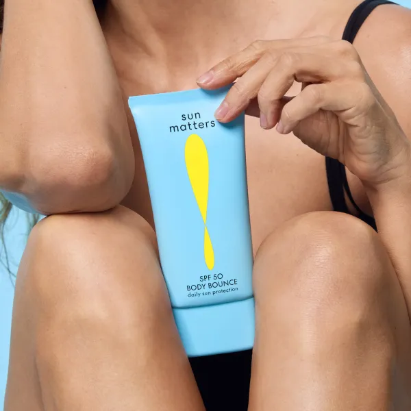 Inimene hoiab naha lähedal käes sinist Sun Matters SPF 50 Body Bounce kehale mõeldud päikesekaitsekreemi tuubi lähivõttes.